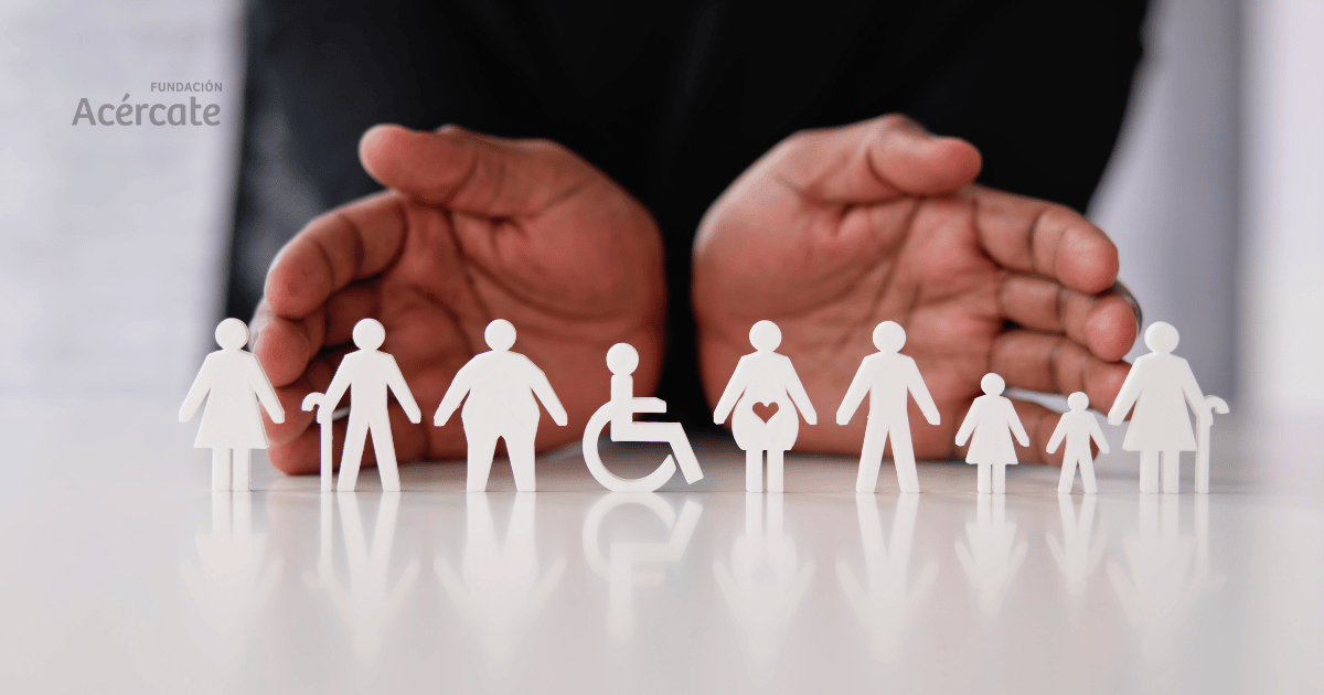 Manos extendidas en gesto protector detrás de figuras de papel blanco que representan la diversidad e inclusión social, incluyendo personas con discapacidad, distintos tipos de cuerpos, géneros y edades. La imagen transmite un mensaje de apoyo, equidad y cuidado dentro de la comunidad. Logo de la Fundación Acércate en la esquina superior izquierda.